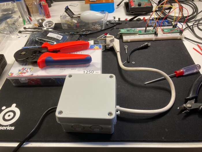 Elektrisk kopplingsdosa med kablar, verktyg och elektroniska komponenter på arbetsbord.