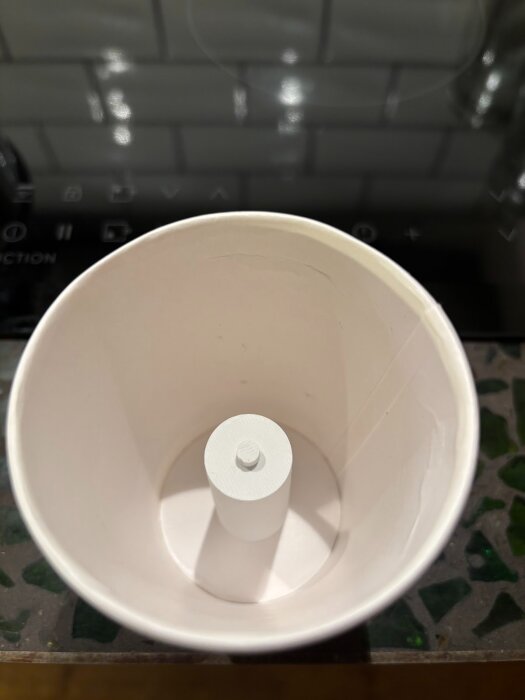 En pappersmugg med en vit cylinderformad insats i botten, använd för att gjuta glasformar.
