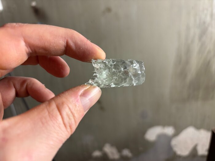 En hand håller en liten, ojämn glasbit, där kanterna är utsträckta och fulla av håligheter efter ett misslyckat experiment.
