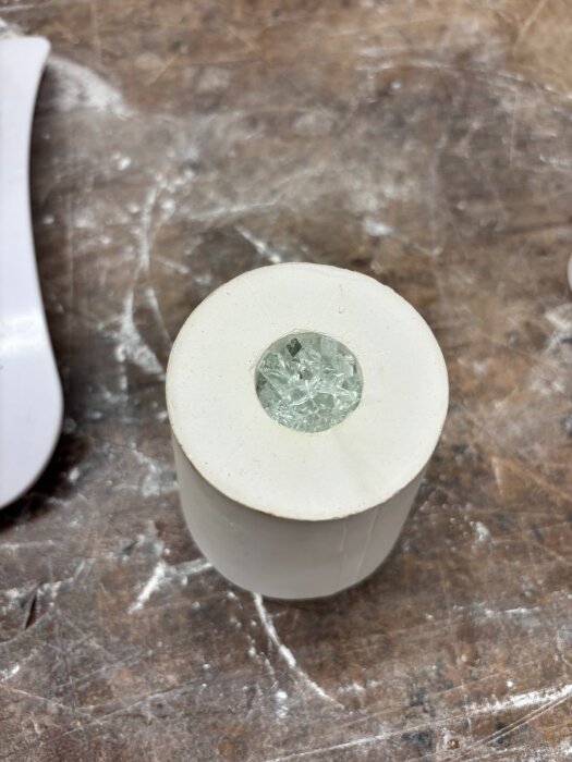 Cylindrisk gipsform med klarglasfragment i öppningen, placerad på en träyta. Formen används för experiment med glasgjutning.