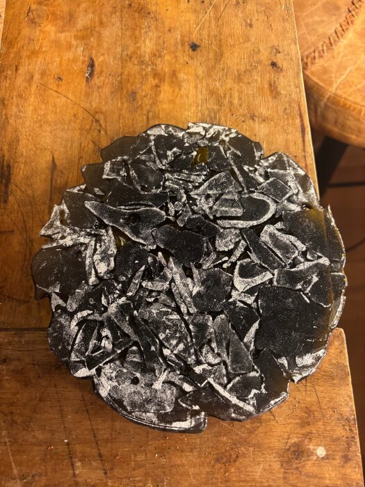 Krossade glasbitar på en träyta, täckta av vita rester, från ett experiment med glasfusion i ugn.