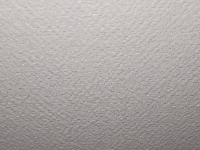 Vit vägg med en grov, texturerad yta, troligen målade eller tapetserade med en typ av strukturtapet.