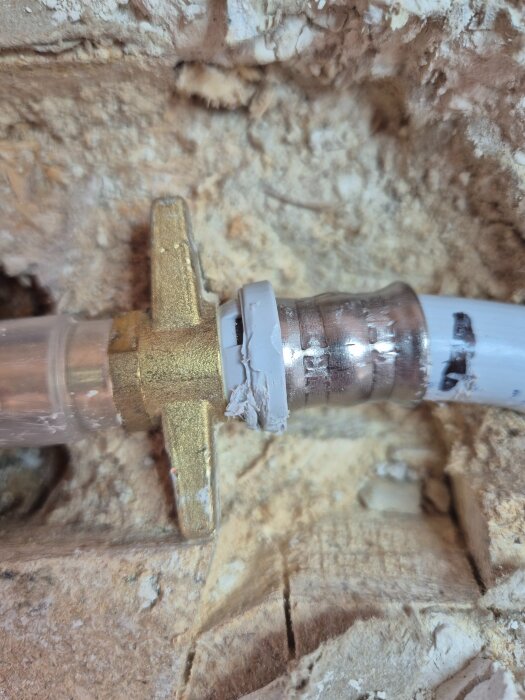 Närbild på rörskarv med metallkoppling och plastslang installerad i ett vägghål.
