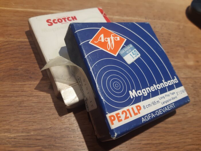 Förpackningar av magnetband från Agfa och Scotch på ett träbord.