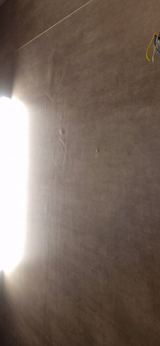 Badrumsväggen efter golvmattans installation och spackling, med en skarv synlig under ljusinsläpp från vänster.