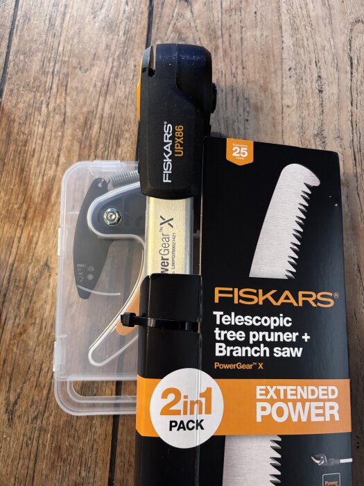 Fiskars UPX86 grensax och såg med teleskopskaft och förpackning, liggande på ett trägolv.
