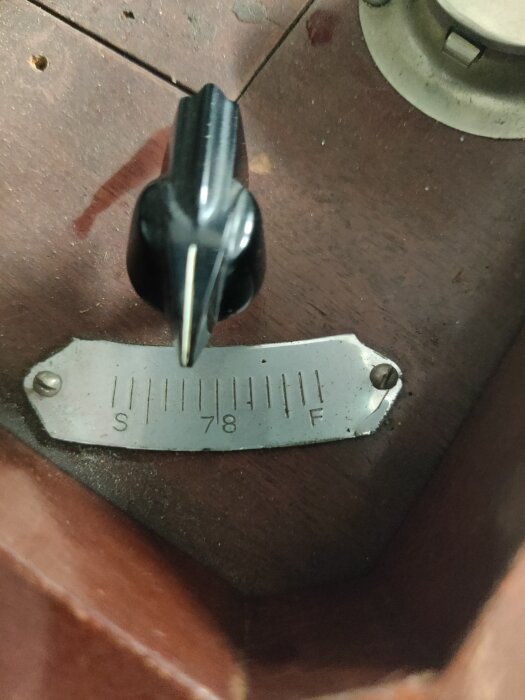 Svart ratt på en träyta med en skala märkt "S", "78", "F", med metallplatta.