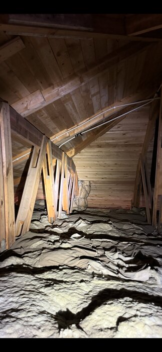 En kallvind med träkonstruktion och råspont syns ovan, med isoleringsmaterial på golvet under takbjälkarna.