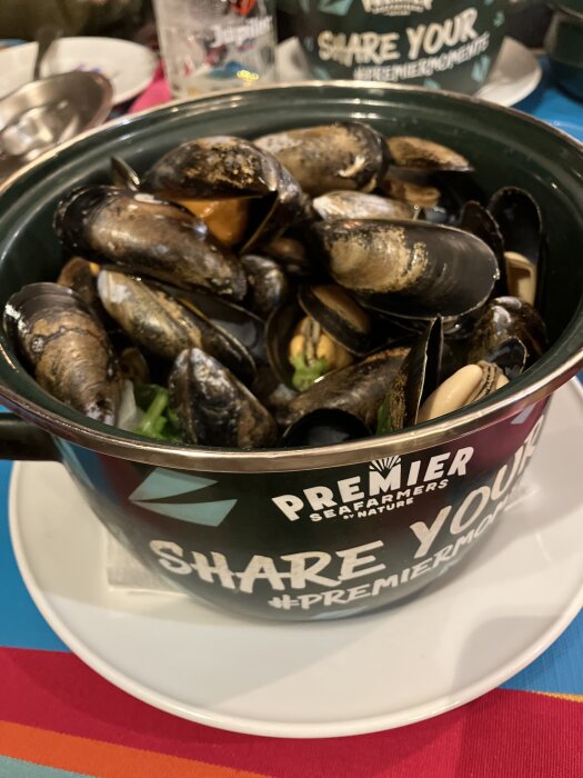 Svart gryta fylld med kokta musslor på ett vitt fat, med texten "Premier Seafarmers" och "Share Your #PremierMoments" på sidan.