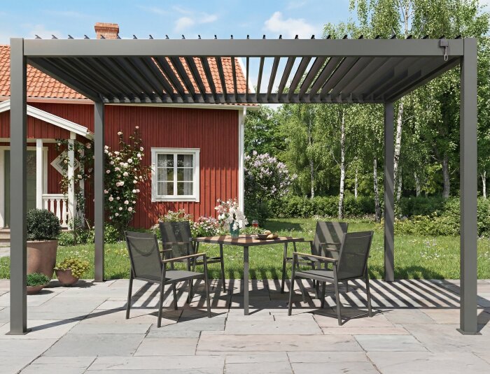 Aluminiumpergola med öppet tak över ett bord och stolar, placerad på ett stenbelagt uteområde framför ett rött hus.