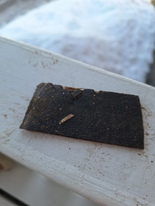 En bit av en mörk papp- eller fibermatta misstänkt för asbest, från ett hus från 1977, ligger på en träyta.