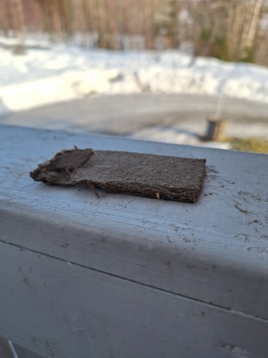 En papp/fibermatta med torkat lim ligger på en yta utomhus, förfrågan om asbestinnehåll i matta som suttit under klickgolv i hus från 1977.