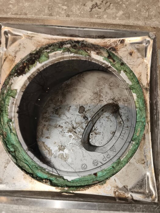 Avloppsbrunn i dusch med smuts och hår runt kanten samt missfärgningar på metallram och tätning.