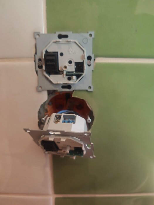 Två monterade termostater i ett kaklat väggutrymme, en av modellerna markerad med "UP", med synlig elektrisk koppling och trådar.