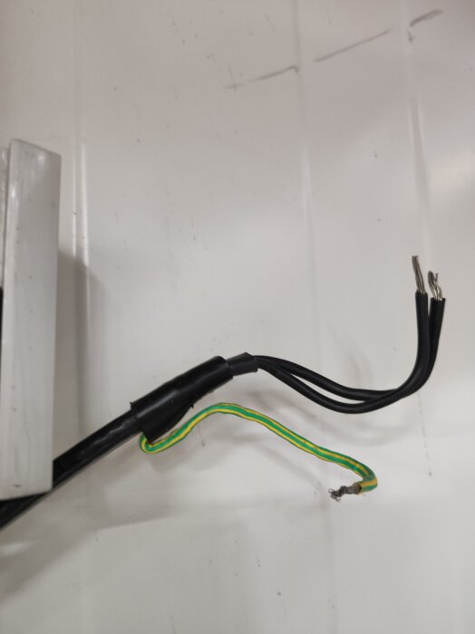 Svart och grön-gul kabel med kapad ände, del av värmekabel till dörrkarm vid byte.