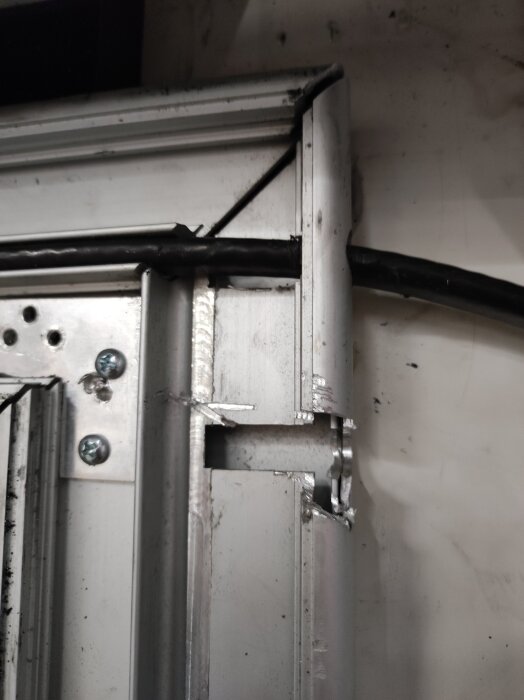 Metallisk dörrkarm med värmekabel och skruvar, skadad yta där kablar behöver friläggas för reparation.