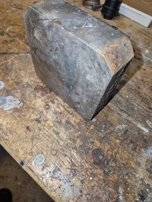 Stor, fyrkantig, rostig metallklump på ett slitet träbord, framtagen vid rensning av en skorsten.