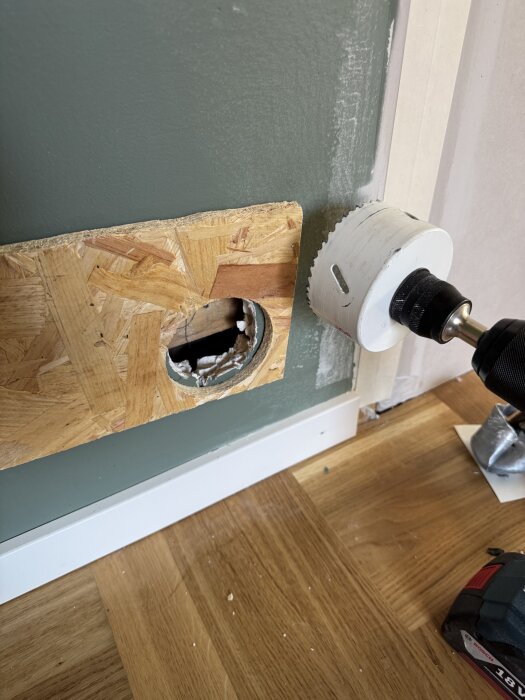 En OSB-skiva på vägg med ett runt hål som borras med dosborr från en borrmaskin vid en renovering.