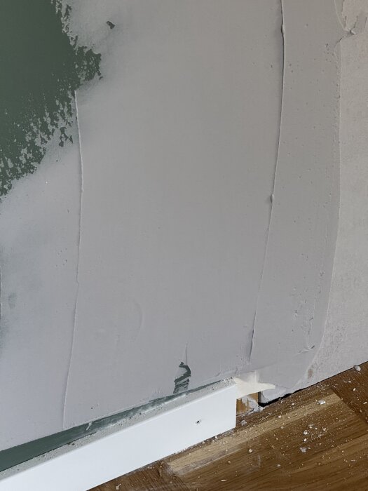 Reparerat väggparti med spackel över ett lagat hål ovanför en golvlist. Synligt sandpapper och ojämn yta.