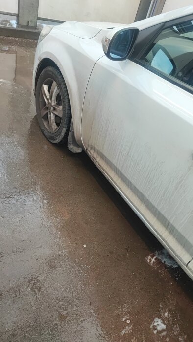 Vit bil med smutsliknande rester på passagerarsidan efter rengöring, stående på vått garagegolv.