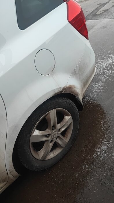 Smutsig bildörr och bakhjul på en vit bil under rengöringsprocessen, synlig rostfläckar och vägsmuts.
