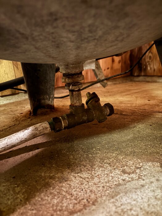 Botten av hydrofor med ventiler och röranslutningar synliga, står på ett betonggolv.