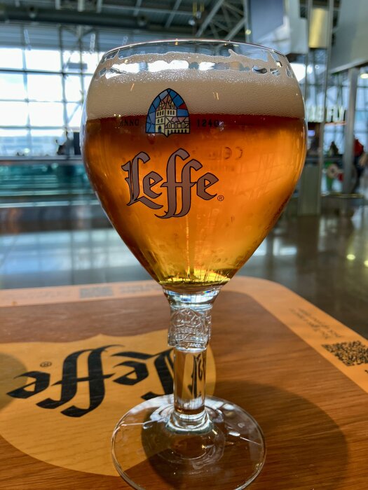 Ett glas med bärnstensfärgad öl (Leffe) på ett bord, i en ljus restaurangmiljö med stora fönster i bakgrunden.