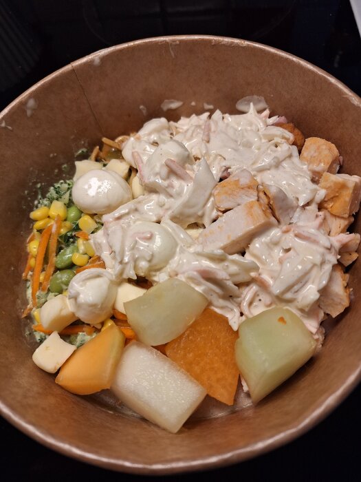 Sallad i en skål med ingredienser som kyckling, ost, melon, broccoli, majs och sås från butikens salladsbar.