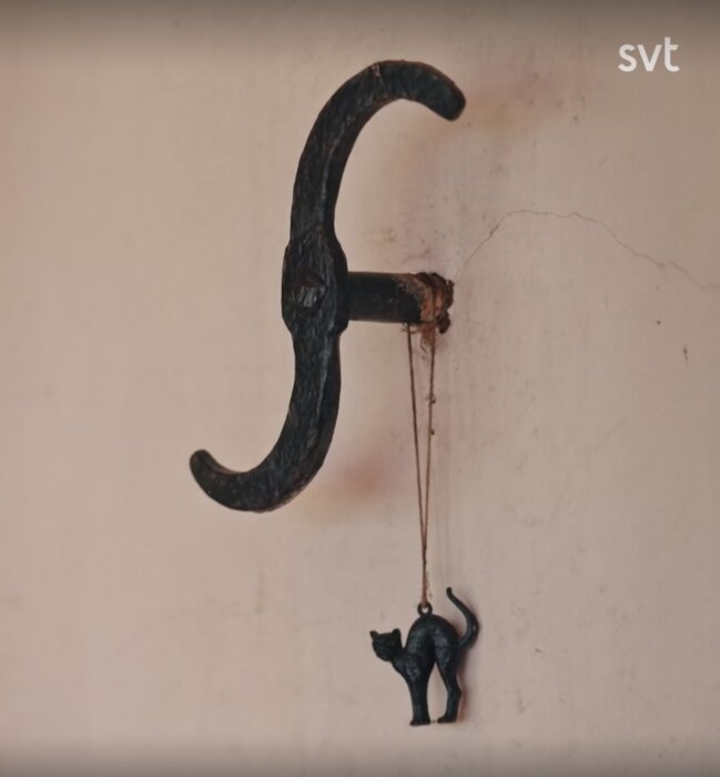 En smideskrok på en vägg med en hängande figur av en svart katt.