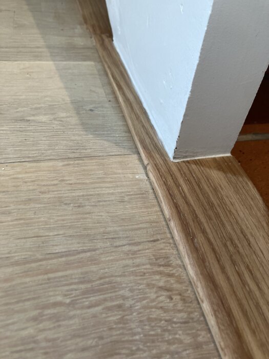 Tröskel i trä mellan kök och vardagsrum, monterad vid vitmålad vägg.