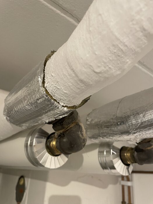 Isolerade rör i taket på en tvättstuga, klädda i vitt material med grått ovanpå, misstänkt för asbest. Huset är från 1959.