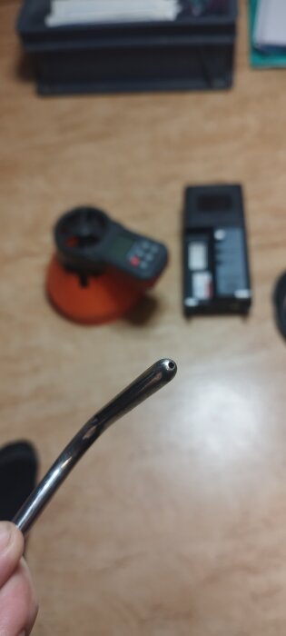 Närbild på spetsen av ett metallrör, suddig bakgrund med mätinstrument på ett bord.