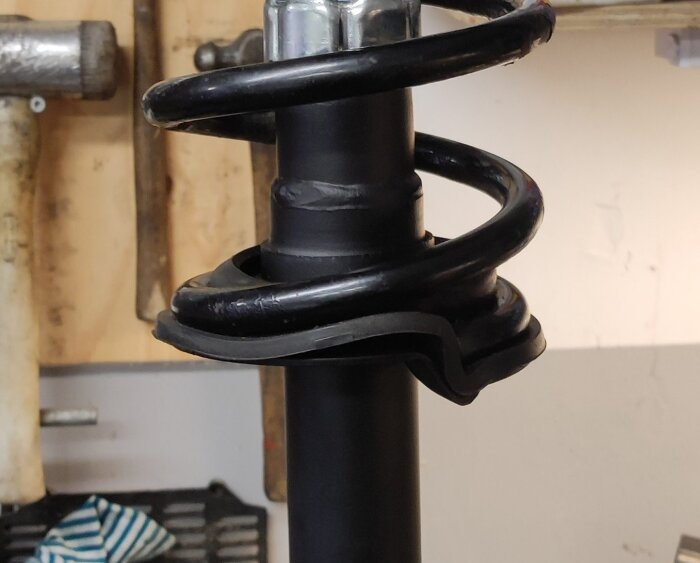 Svart fjäder monterad på bilstötdämpare i ett garage, med verktyg i bakgrunden.