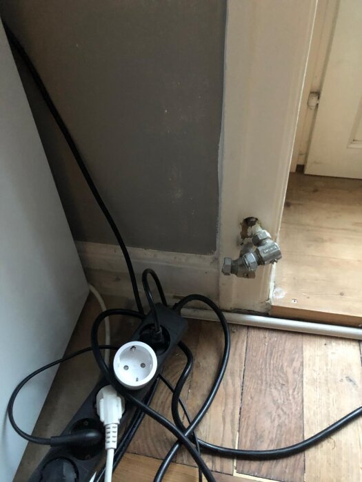 Vägguttag och elkablar framför en grå vägg, med ventiler på väggen som visar platsen där ett element tidigare suttit.