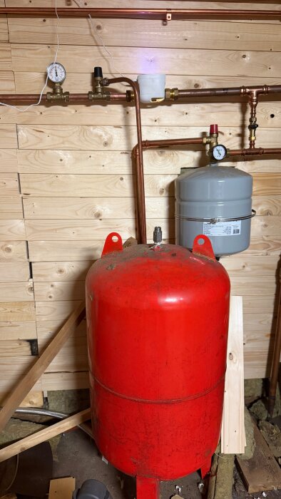 Röd Zilmet-hydropress och grå trycktank installerade mot en träpanelvägg, kopplade med kopparrör och tryckmätare.