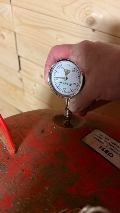 Man mäter trycket på en röd hydropress med hjälp av en tryckmätare, som visar cirka 3,6 bar.