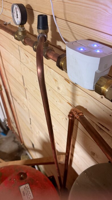 Hydropress med manometer och rörledningar i ett pumprum. Manometern visar trycket och kopplingarna är av koppar och mässing.