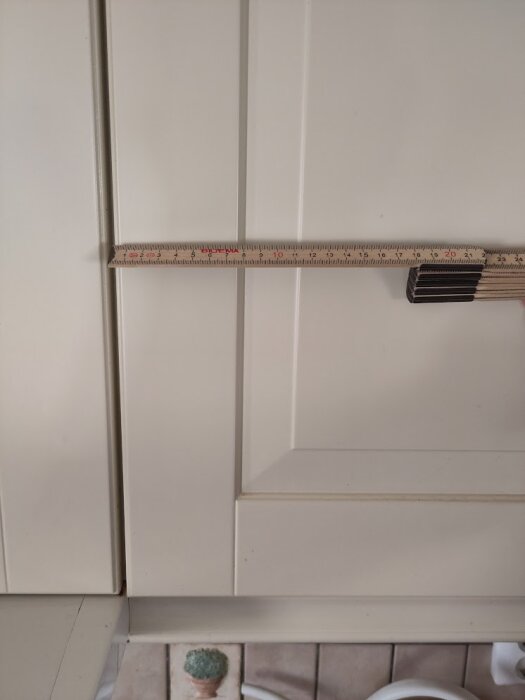 Linjal mäter avstånd mellan vita skåpdörrar i kök.
