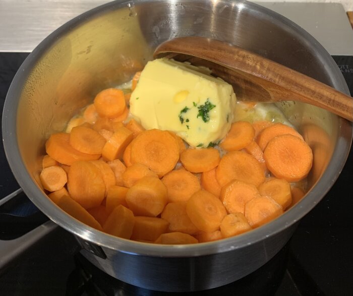 Morotsskivor och smör smälts i en kastrull på spisen med en träsked.