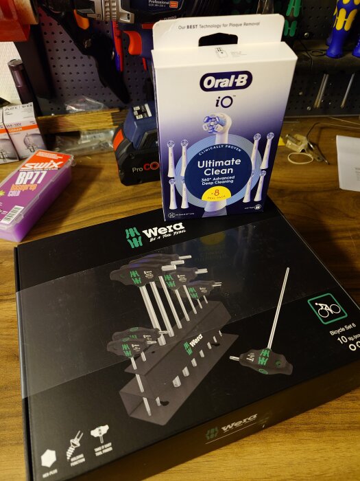 Förpackning med Oral-B tandborstrefiller och Wera verktygssats på ett bord i en verkstadsmiljö.