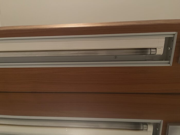 Lysrör i en badrumsspegel från Vedum, inramat i trä med metallkanter.