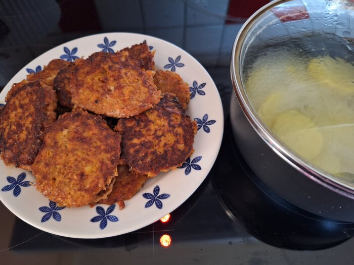 Morotsbiffar på en vit tallrik med blå blommor bredvid en kastrull med kokande potatis.
