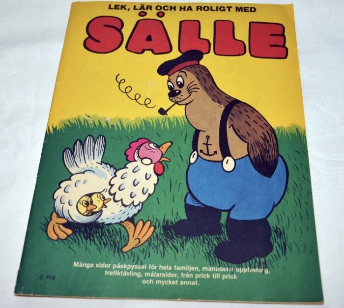 Illustrerad tidningsomslag med texten "Sälle". Tecknade figurer: en säl i byxor och en höna på gräsmatta.