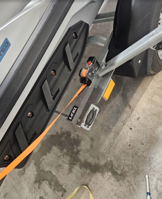 Automatiskt återrullande spännband monterat på en vattenskotertrailer, med orange band fäst vid skoterns plattform.