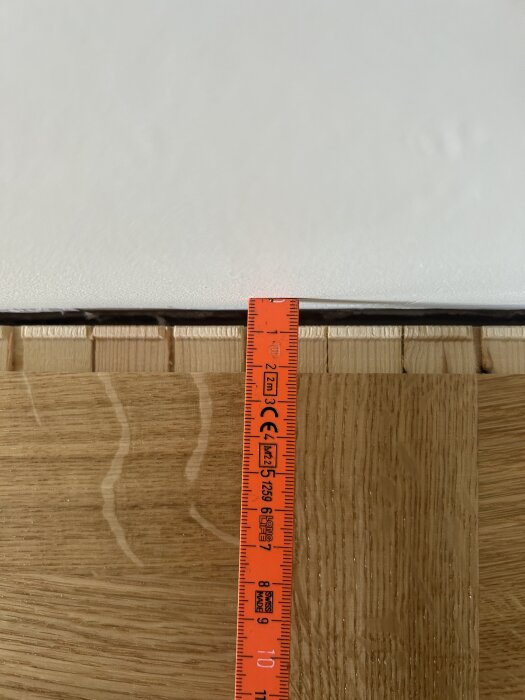 Parkettgolv installerat med en synlig glipa mot väggen, mätt med ett rött måttband.