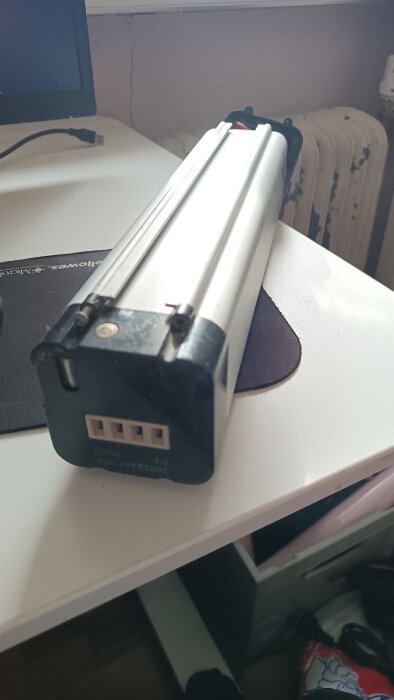 Bild på ett Ecoride-cykelbatteri som ligger på ett bord. Batteriet har en metallhölje och flera anslutningar på en av sidorna.