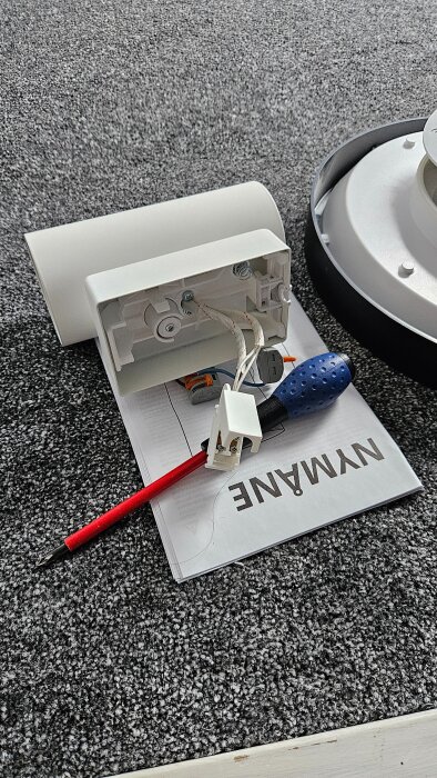 Trasig lampa från Ikea med skruvmejsel och kablar, ligger på en manual på en grå matta.