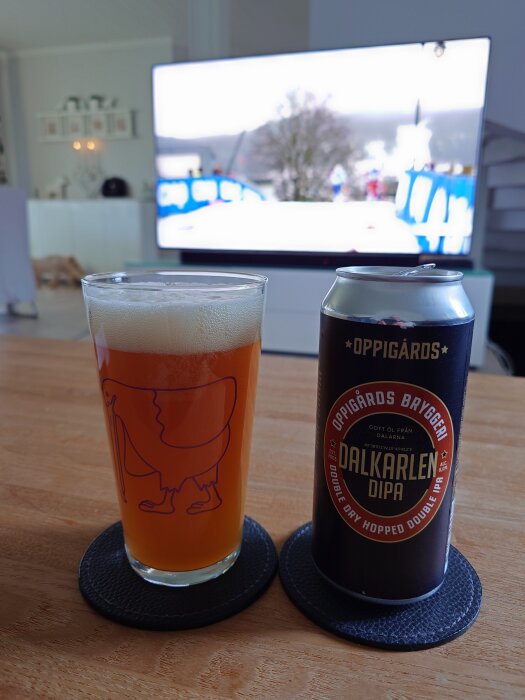 Ett glas med daladricka och en burk Oppigårds Dalkarlen DIPA på ett bord framför en TV som visar skidsprint.