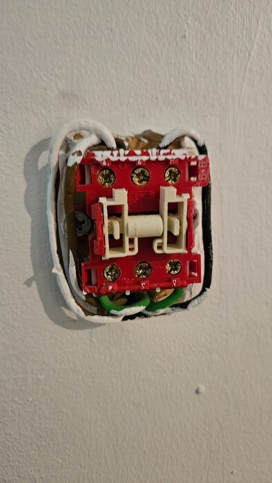 Elektrisk brytare med synliga ledningar monterad i en vägg, delvis avtäckt med röd och vit komponent.