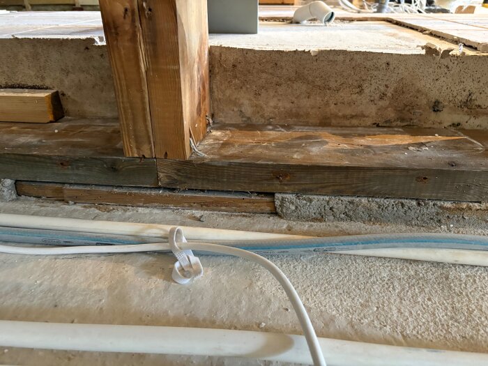 Bärande träsyll på betongplatta med kablar i förgrunden och en träregel ovanpå, del av renovering i översvämningsskadad källare.